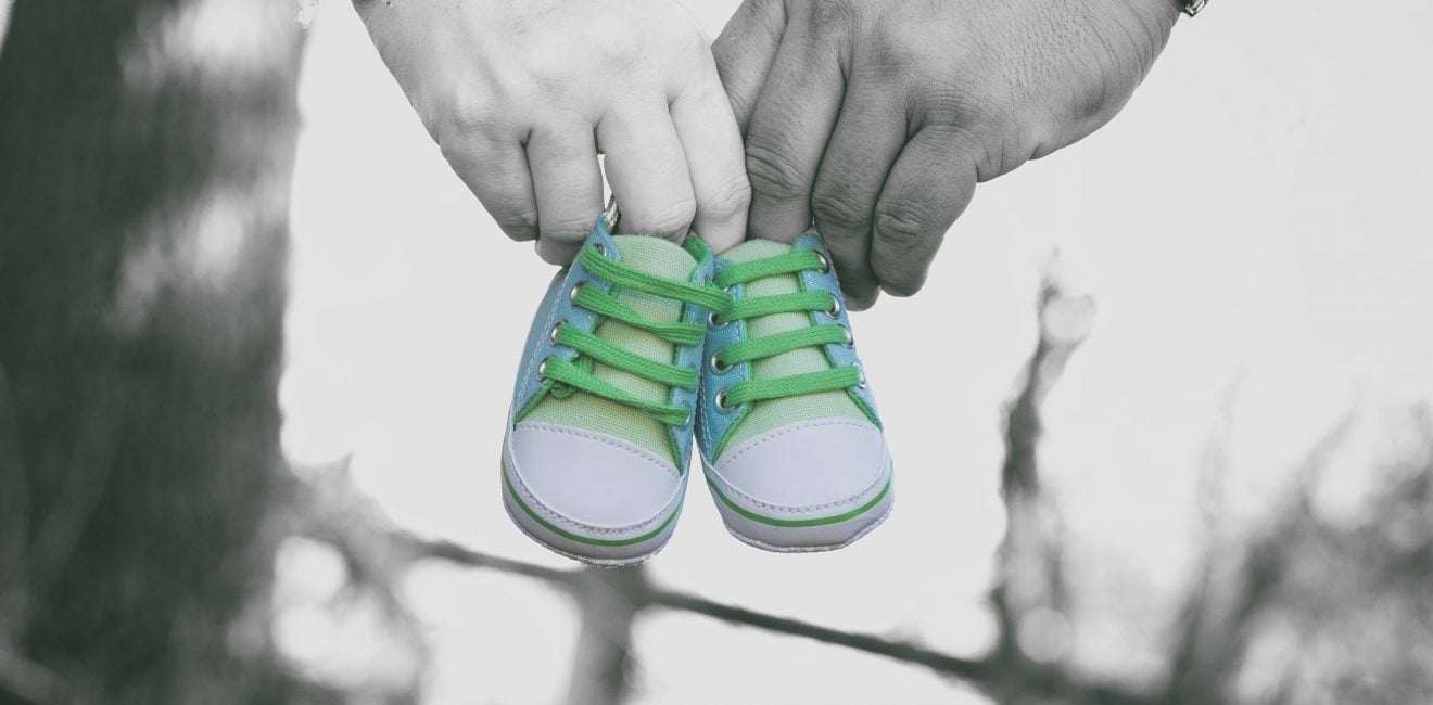 Parent Employee Rights | Parental Leave | Close up of a couple's hands carrying a pair of baby shoes