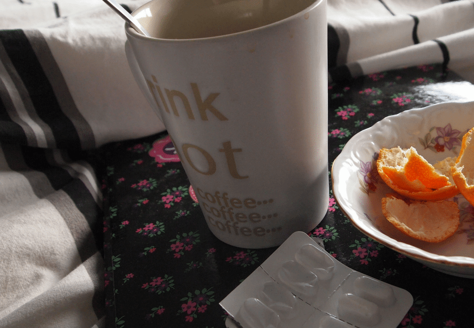 Sick leave | coffee cup, orange peels in a plate next to medicine on a bed