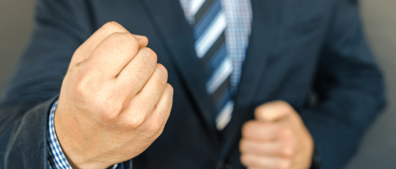 bullying | Torso of a man in a suit with clenched fist in the foreground